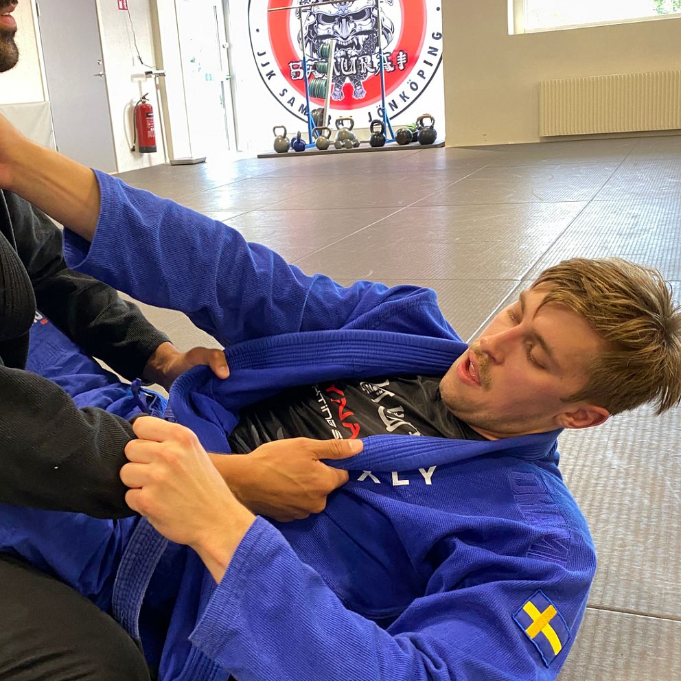 två män, en i svart klädsel och en i blå, brottas i sporten brasiliansk jiu-jitsu