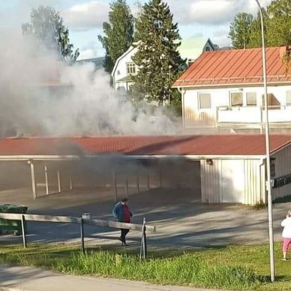 Det ryker från en graragelänga som brinner. Människor står och tittar.