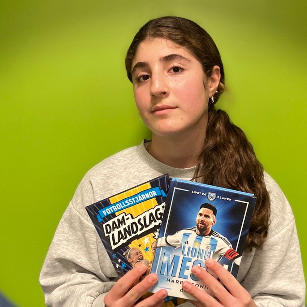 En person håller upp två böcker, en om damlandslaget i fotboll och en biografi om Lionel Messi. Bakgrunden är grön och personen bär en grå tröja.