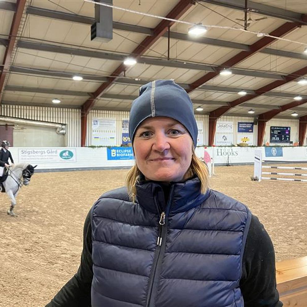 Tävlingsledaren för ponny- children SM i hoppning på Sundsvalls ridklubb 2024, Josefine Wilhelm står i ridhuset med hinder bakom sig.