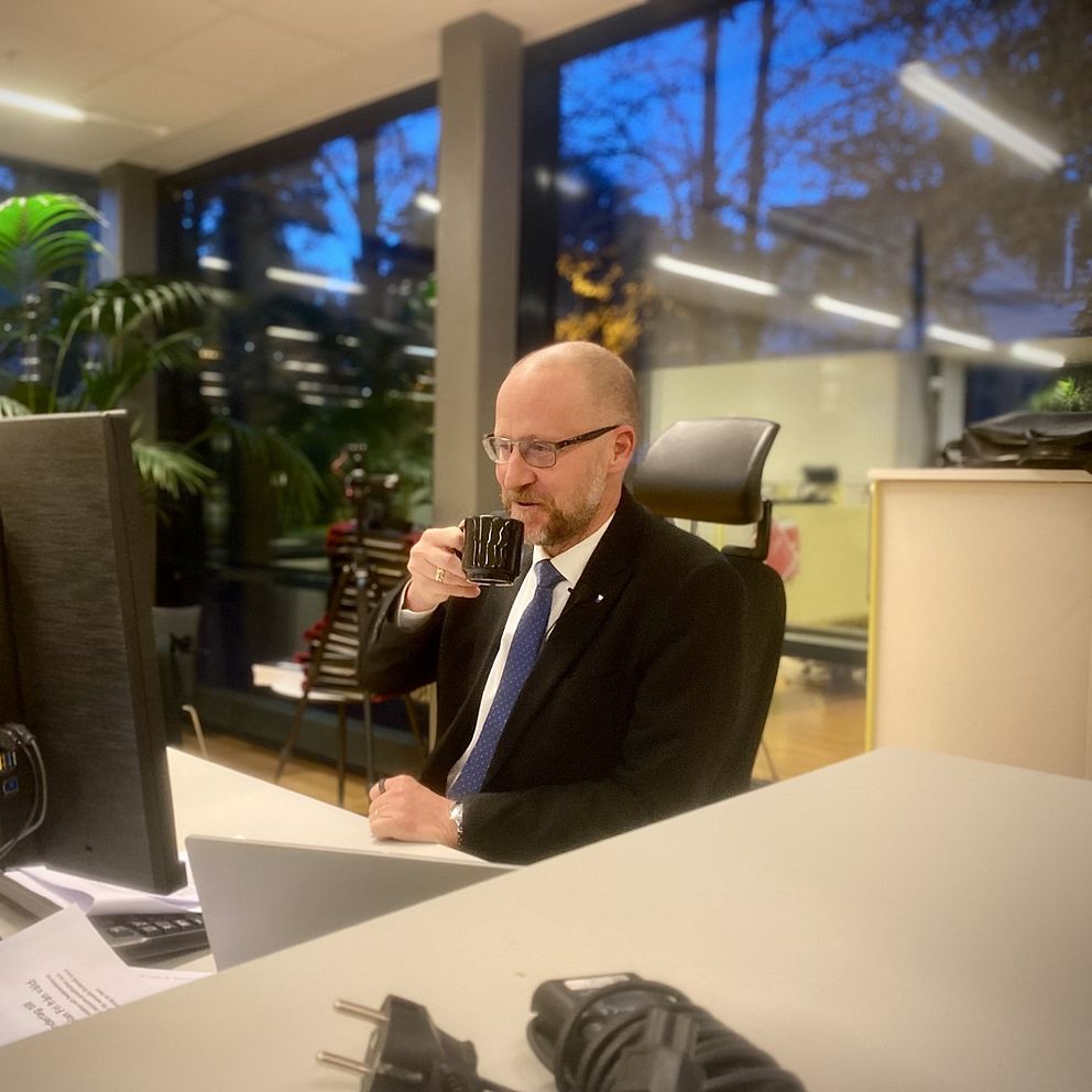 En man i glasögon sitter vid ett kontor och dricker kaffe