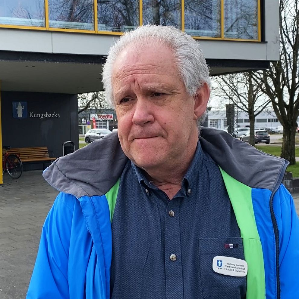 Person i blå jacka framför byggnad med gul dörr och glasfönster.