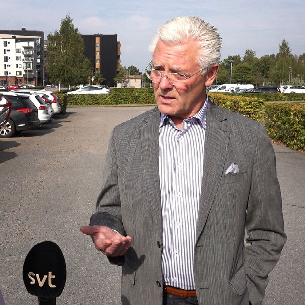 En man med grå kostym står på en parkering och pratar