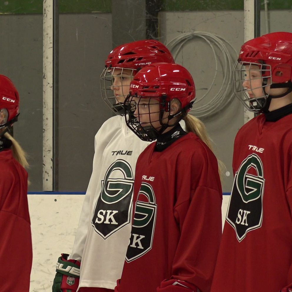 Flera tjejer står i hockeykläder och tittar ut från bild