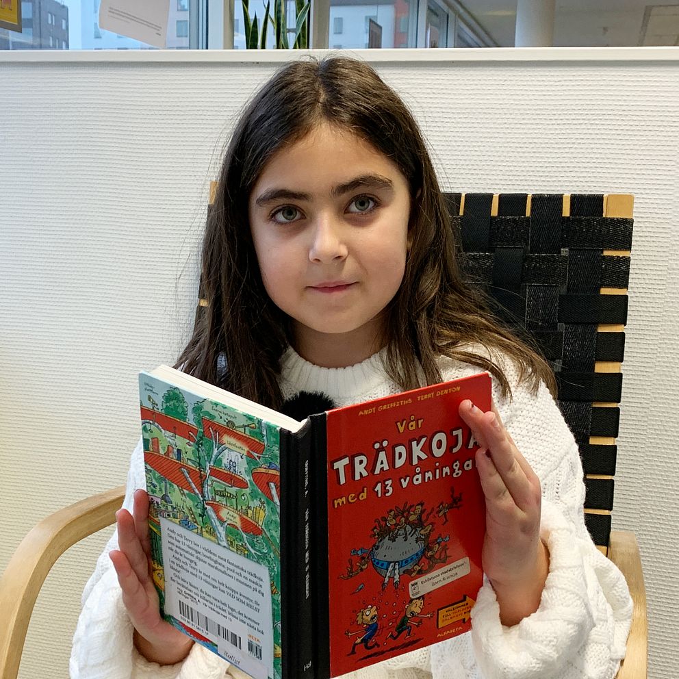 En flicka sitter i en fåtölj och läser.