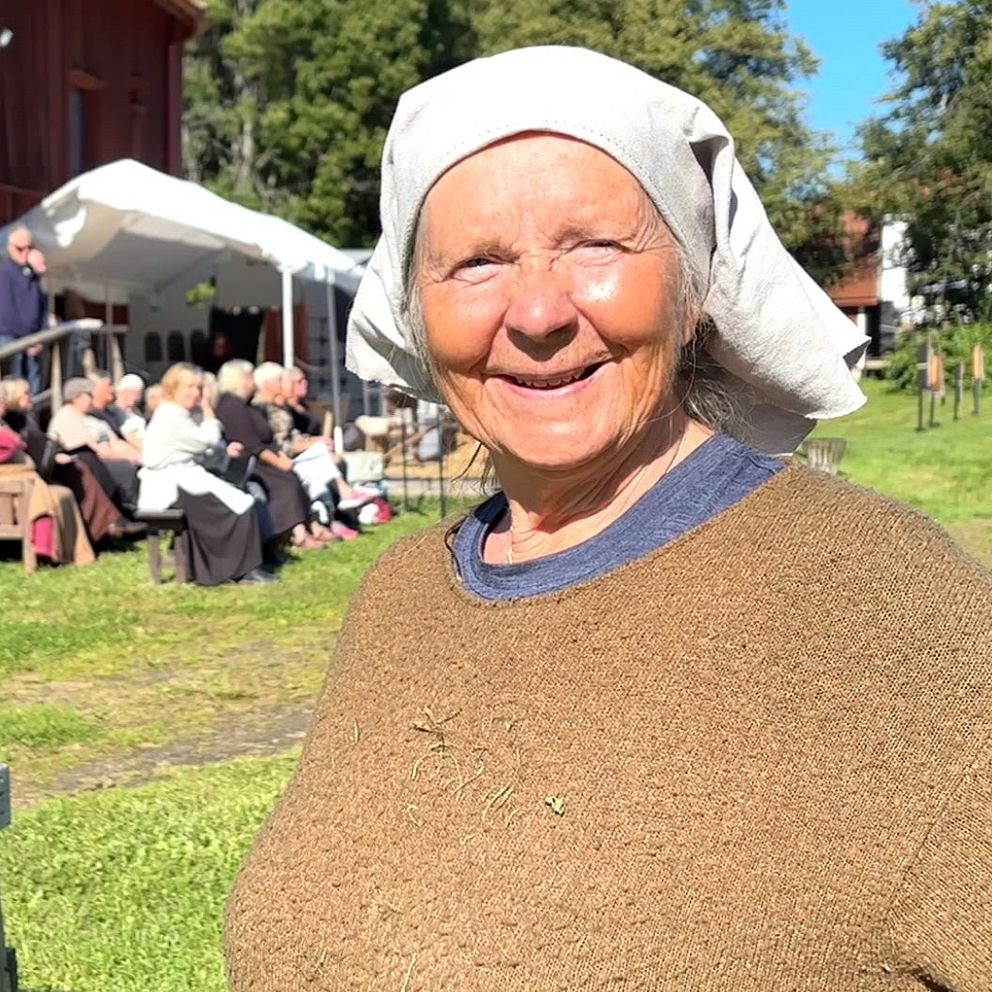 Gunilla Ojala i kostym utomhus vid teaterföreställningen ”Märgit” med publik i bakgrunden