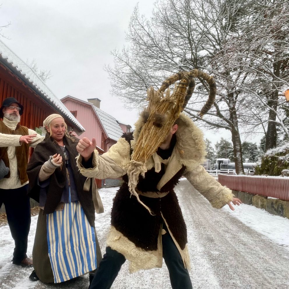 En julbock hålls fast i ett rep av en man och en kvinna i gammeldags kläder.