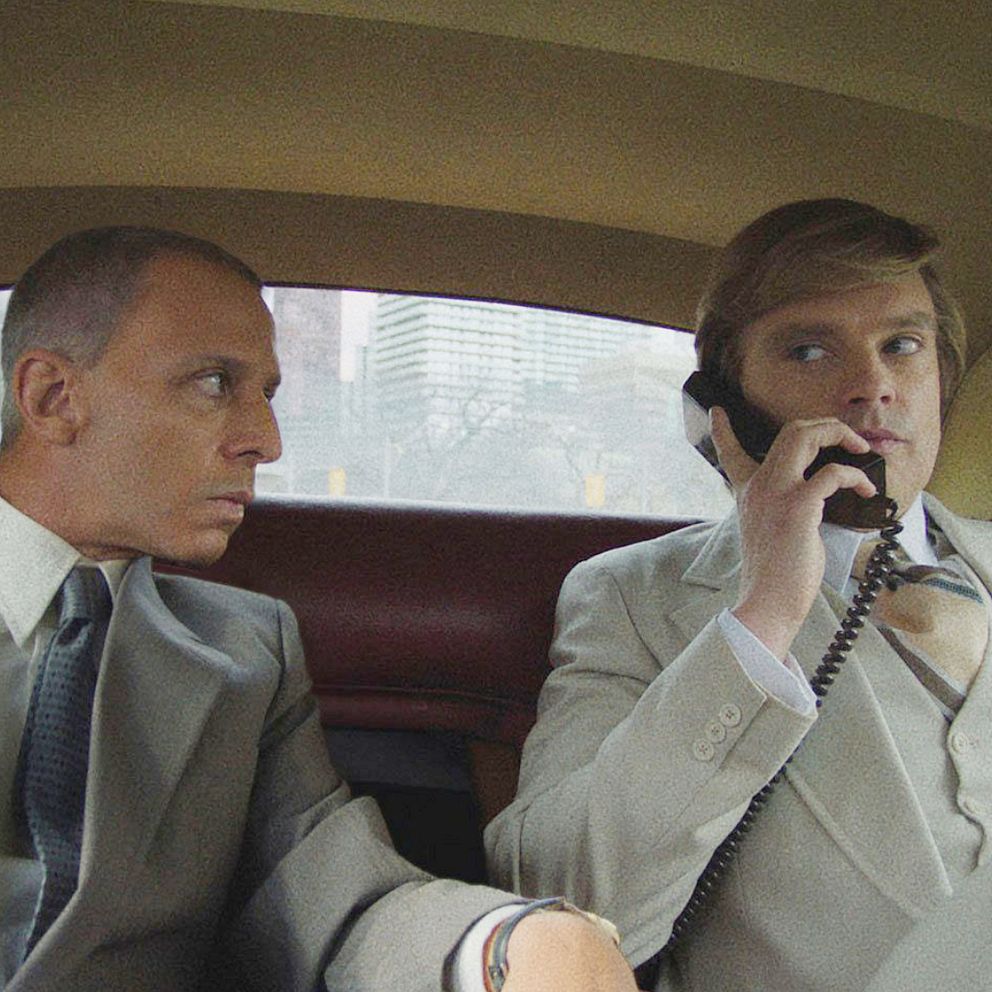 Bildens vänstra del visar en person i en svart kostym med vit skjorta och orange fluga, stående i en modern miljö. Höger del av bilden visar två personer i en vintageinspirerad bil, iförda grå kostymer och pratar i telefon. Båda sektionerna framhäver olika stilar och miljöer, den ena modern och den andra retro.