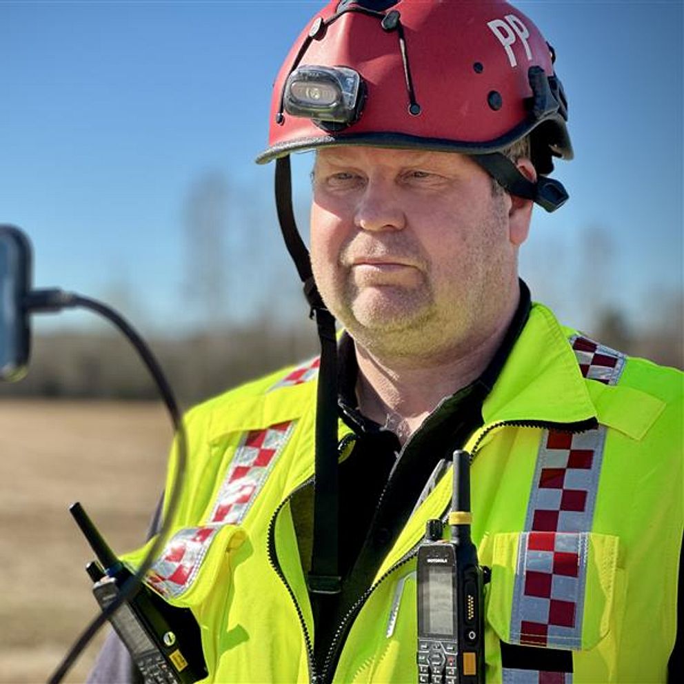 Brandman i hjälm med radioutrustning testas utomhus med mobiltelefon.