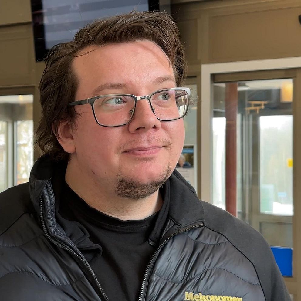 Vakt i svart jacka står i en entré vid glasdörrar och fönster.