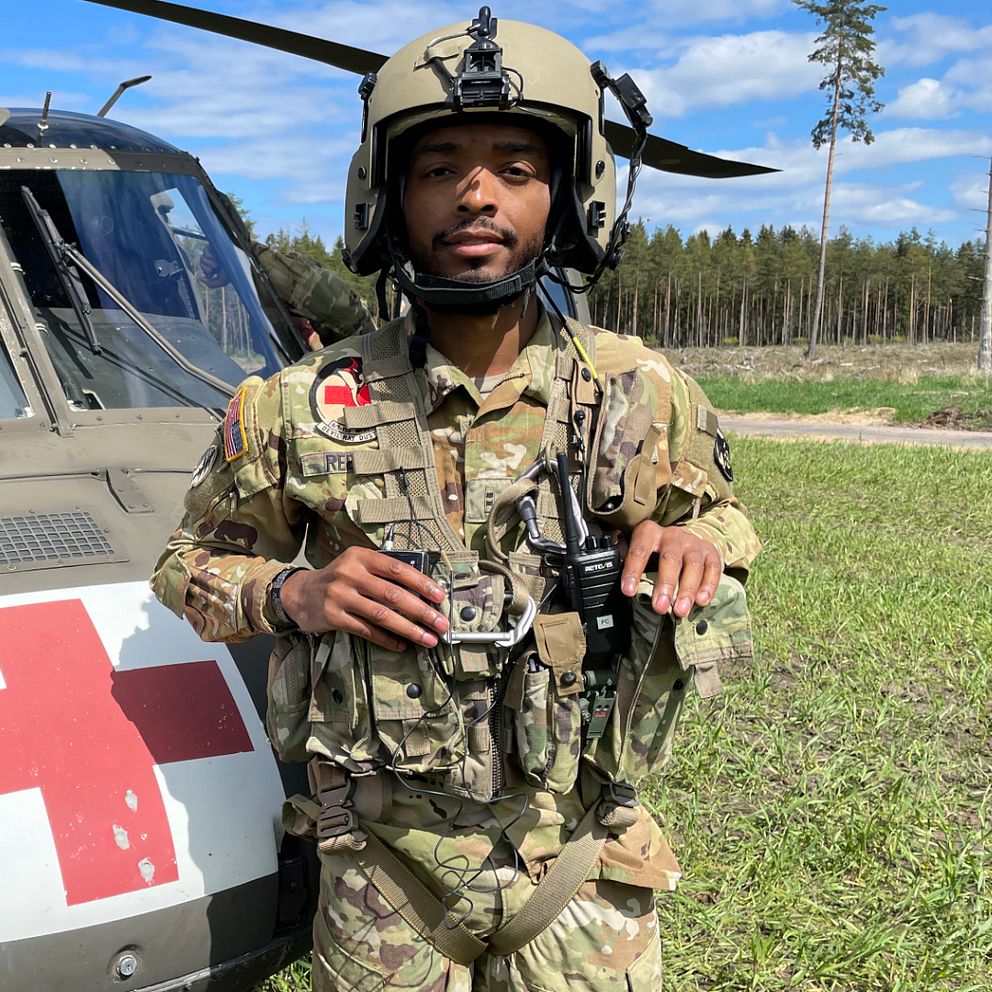 En ung man står i militära kläder framför en Blackhawk helikopter.