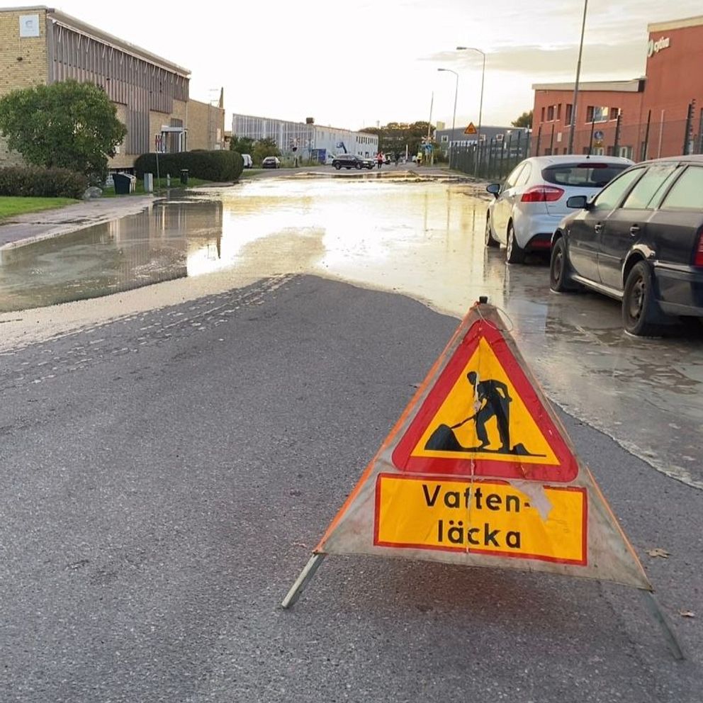 Vägskylt vattenläcka framför översvämmad gata.