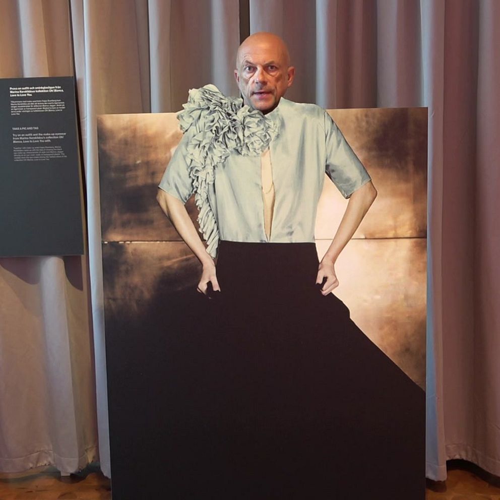 Till vänster finns en person i en inomhusmiljö med en konstnärlig bakgrund som inkluderar målningar. Personen bär en pärlsmycke. Till höger syns en stor målning av en person i en elegant outfit med en blommig detalj på axeln, uppställd i en utställning med informationstavlor i bakgrunden.