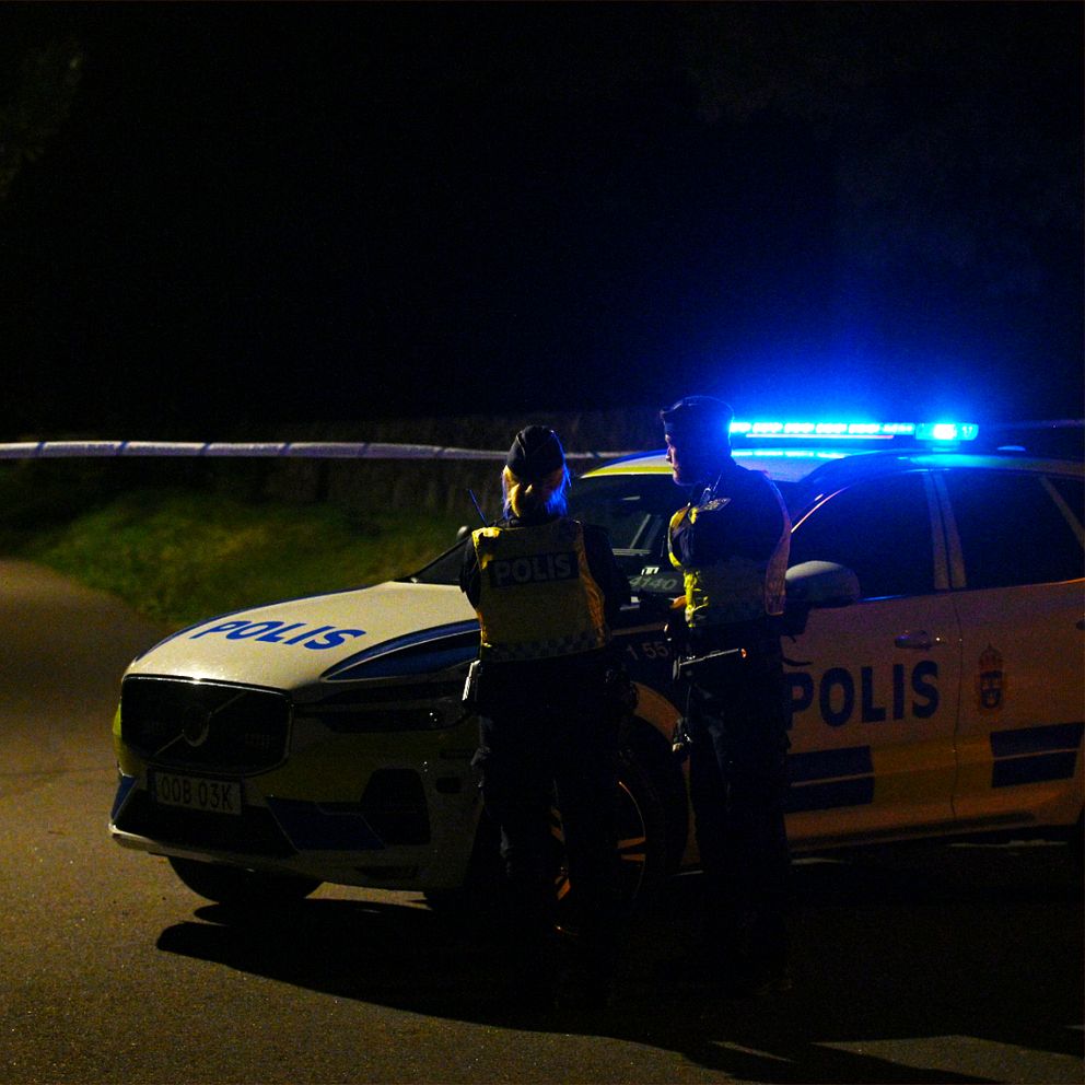 SVT-reporter på plats. Polisbil i mörker vid Skogskyrkogården i Falkenberg