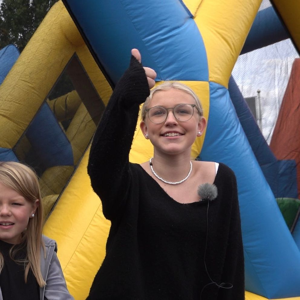 Tre tjejer framför en hoppborg. Den ena tjejen gör tummen upp.