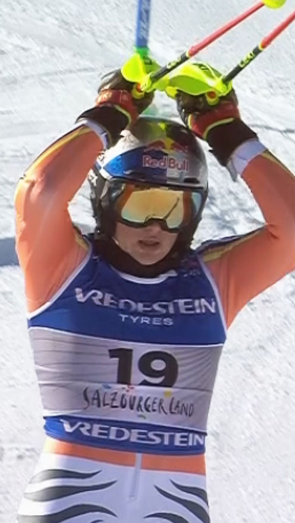 En delad bild visar en skidåkare med tävlingsnummer 19 i en slutposition med stavarna ovanför huvudet och en skidåkare med nummer 29 som ramlat på snön under en skidtävling.