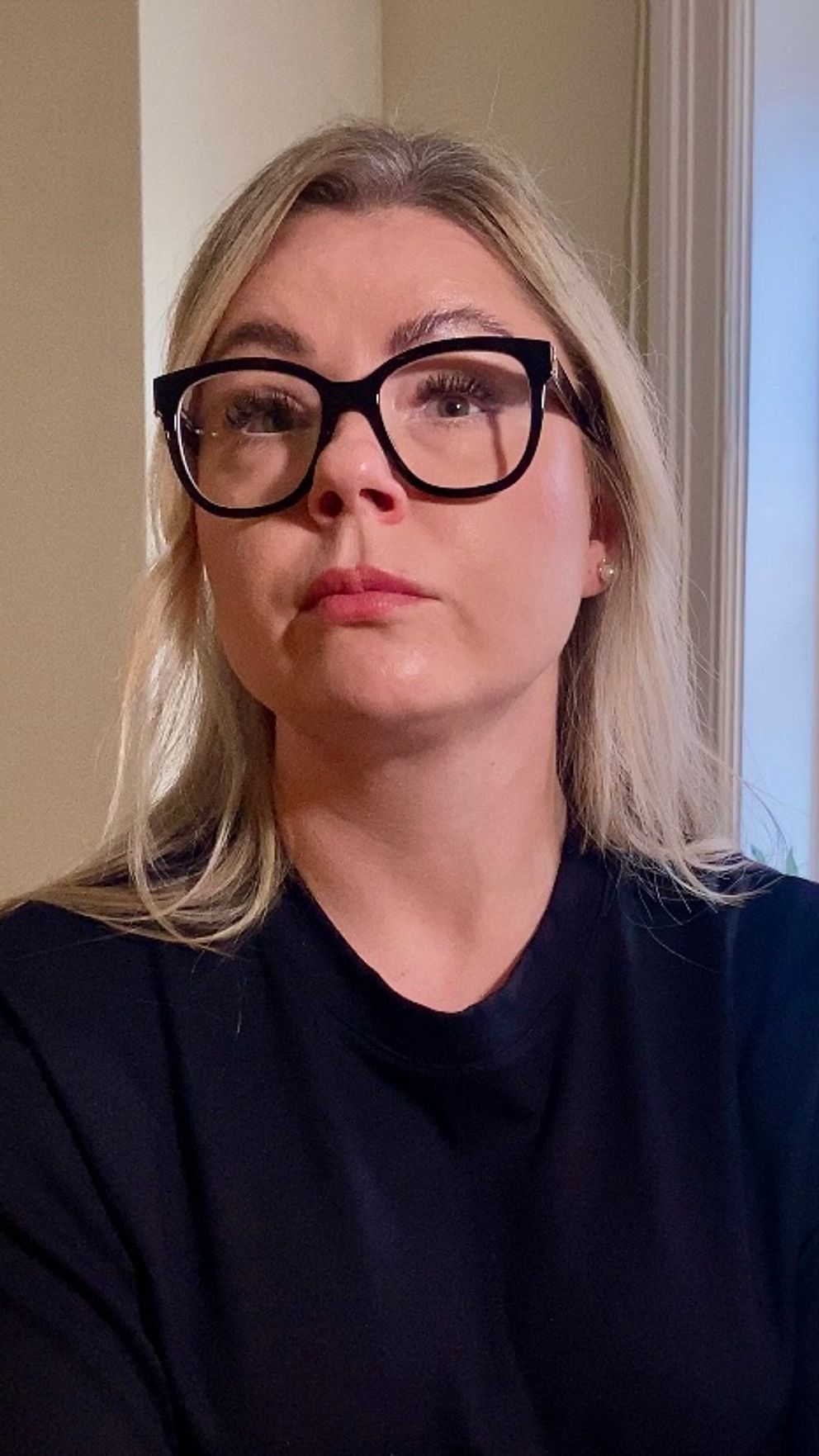 Sara Blixt sitter i ett rum med armarna i kors framför ett fönster med växter.