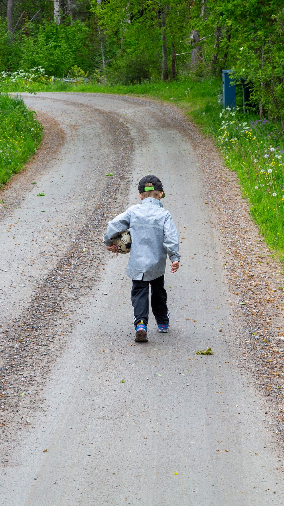 Barn går ensam på grusväg i grön skogsmiljö