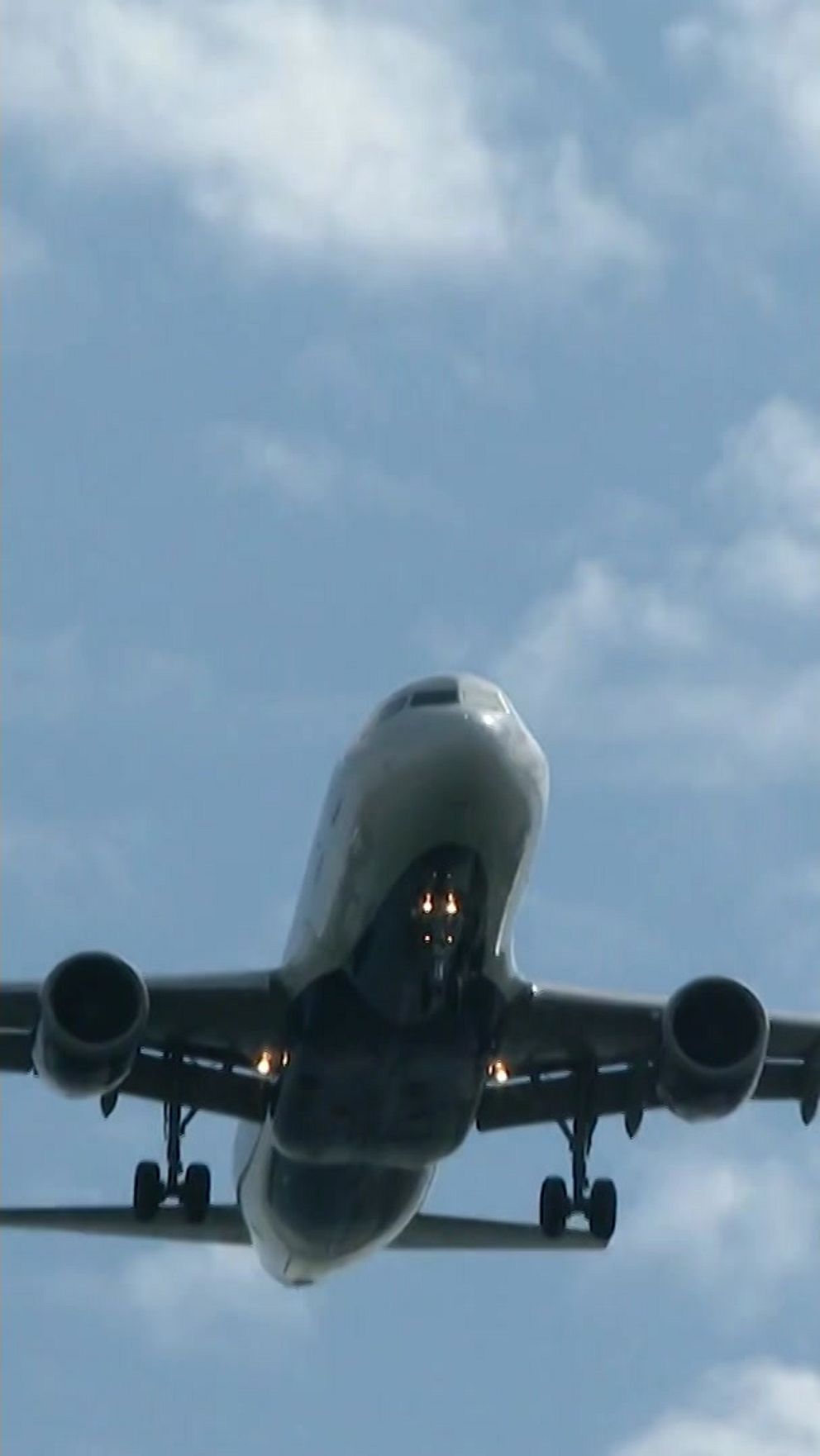 Ett flygplan flyger lågt genom en klar himmel med några moln i bakgrunden.