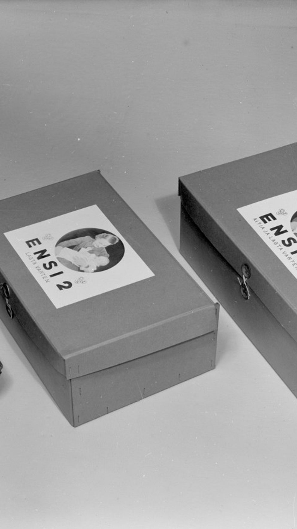 Vuoden 1938 kolme erilaista äitiyspakkausta. Kaksi pieniä pahvilaatikoita, yksi ”käärö”.