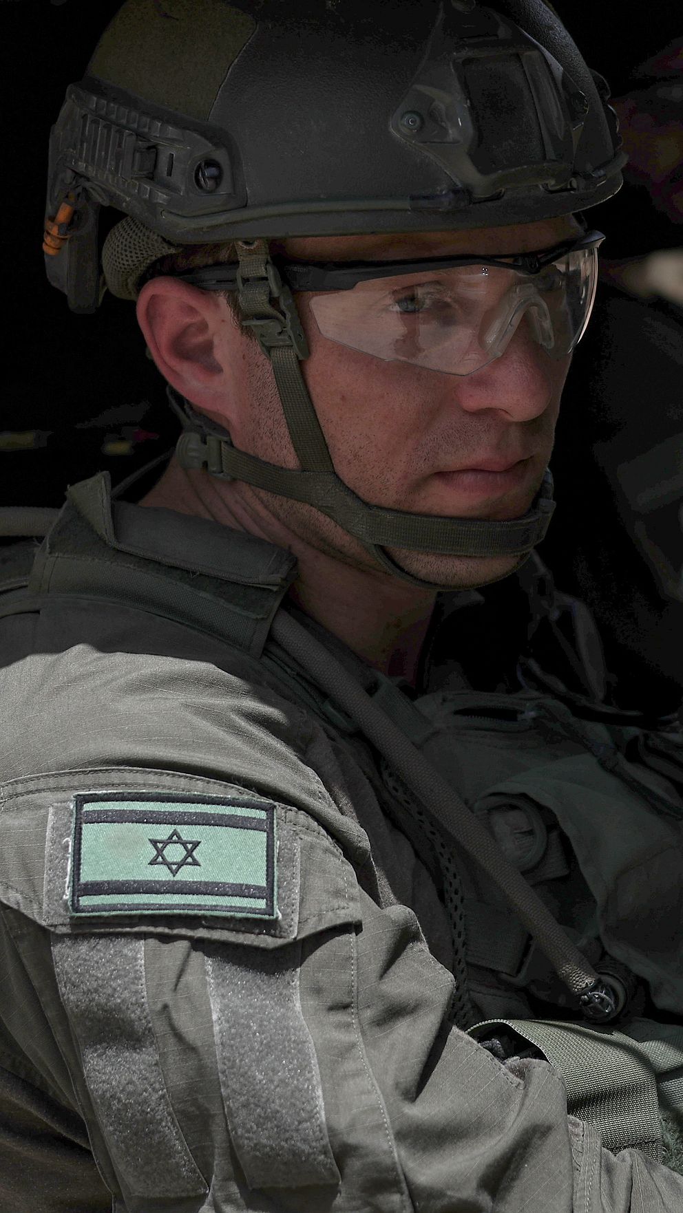 En israelisk soldat sitter i en militärfordon med en ryggsäck och bär en uniform med en israelisk flagga på ärmen.