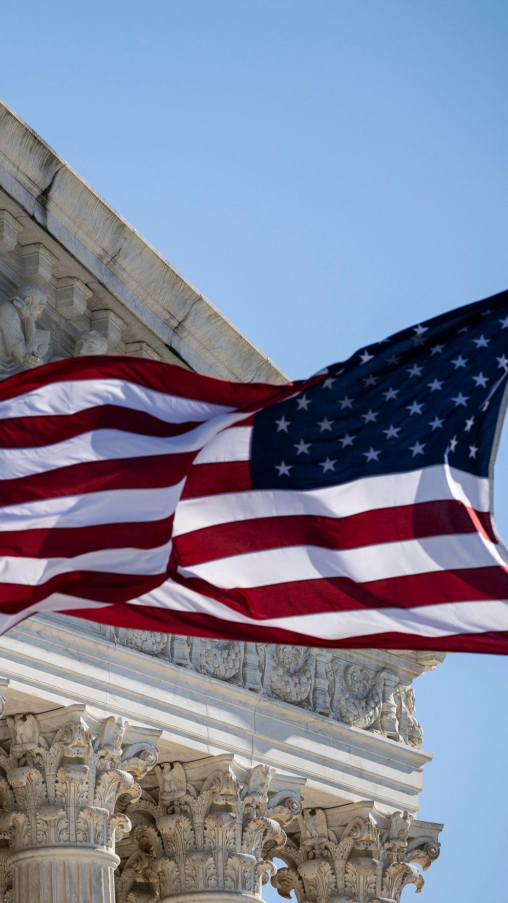 ALT-text: Framsidan av USA:s högsta domstol med detaljerad skulpturdekoration och en amerikansk flagga som vajar i förgrunden. Texten ”EQUAL JUSTICE UNDER LAW” kan tydligt ses ovanför ingången.