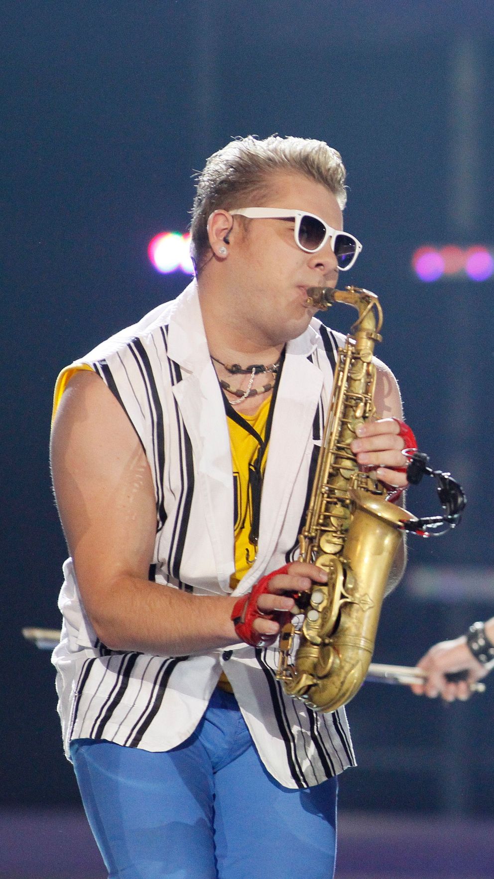 Artist i färgglada scenkläder uppträder på en upplyst scen, med saxofon.