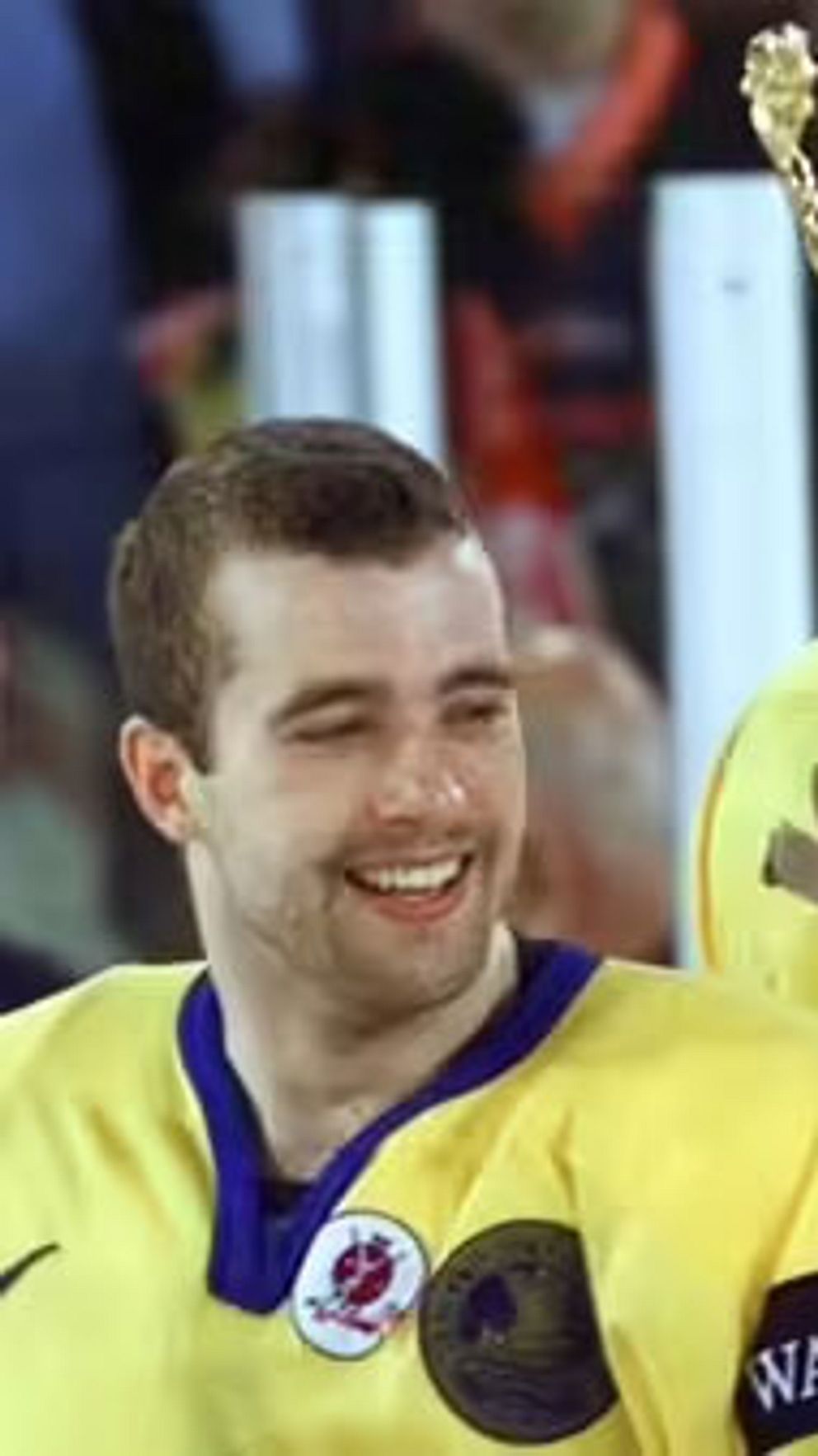 Ishockeyspelare i svenska landslagströjor håller upp en stor pokal efter seger.