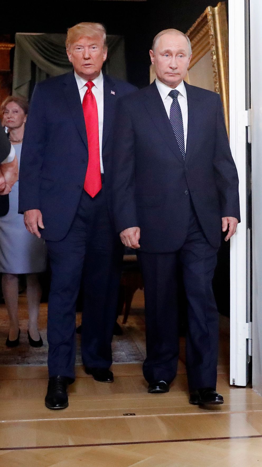 Donald Trump och Vladimir Putin går sida vid sida genom en dörröppning med en uniformerad vakt som håller dörren öppen.