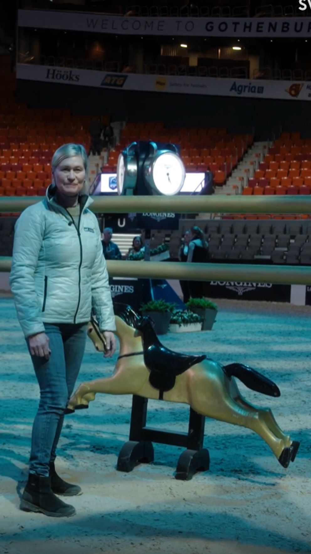 Person står bredvid en mekanisk häst i en arena med tomma läktare.