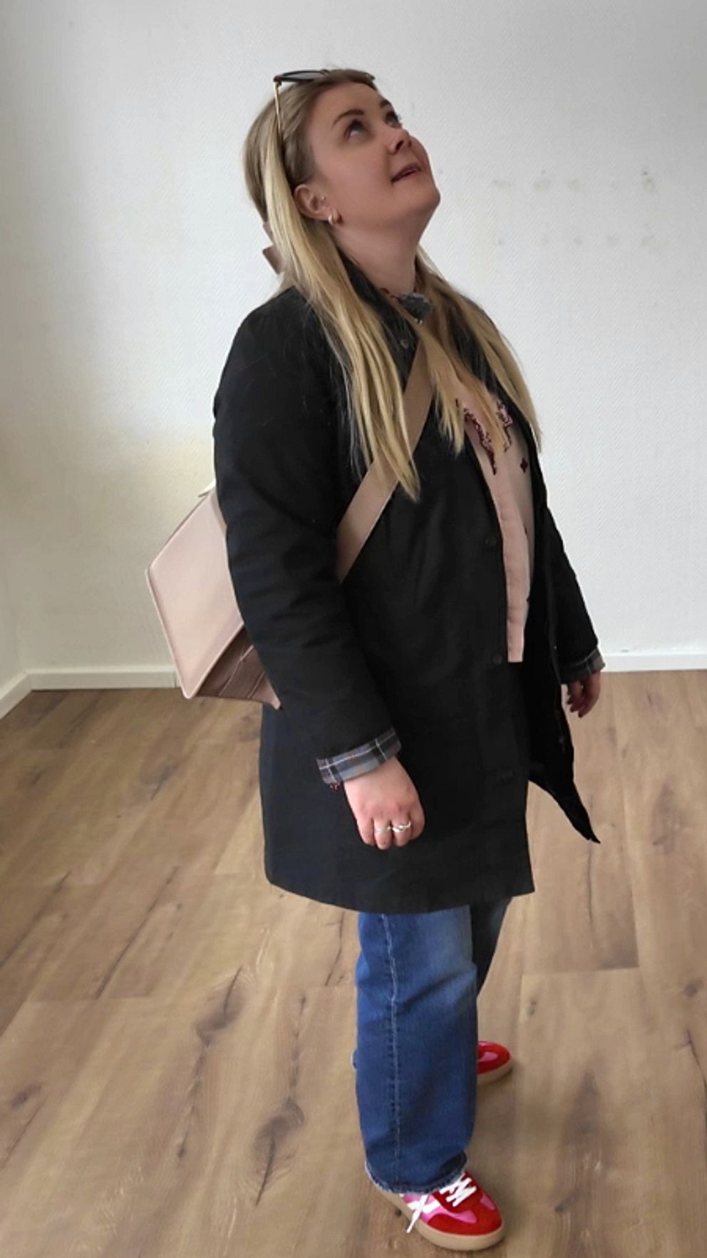 Rebecka Perä undersöker interiören i ett tomt rum med trägolv och vitmålade väggar.