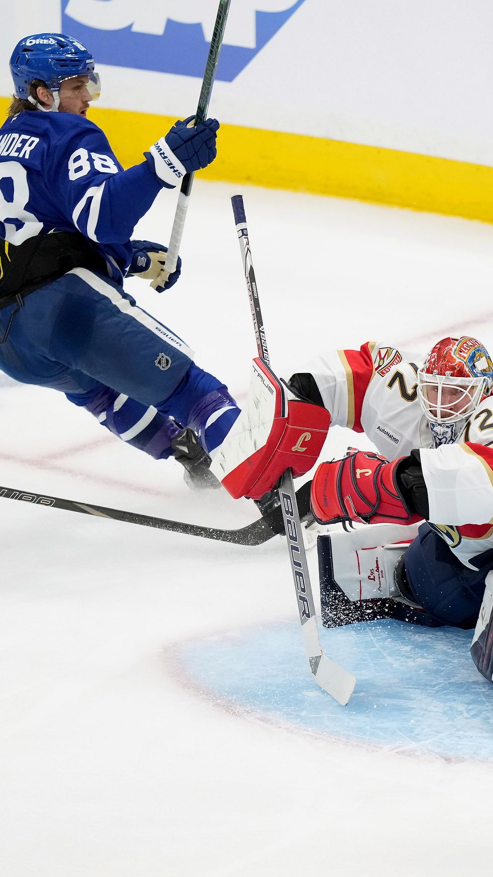 Ishockeyspelare skjuter mot mål där målvakt och försvarare försöker rädda pucken.