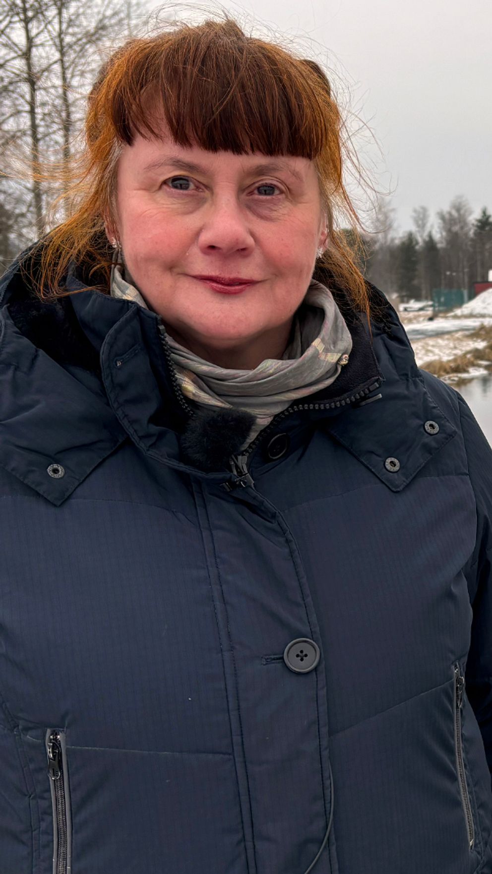 En kvinna i vinterjacka står vid några mindre vattendammar utanför ett reningsverk.