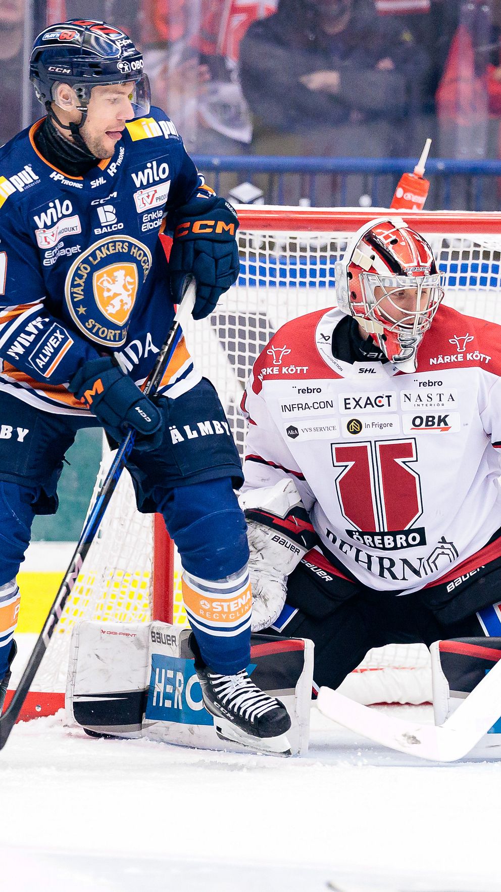 Ishockeyspelare skjuter mot målvakt från motståndarlag, spänning vid målbur.