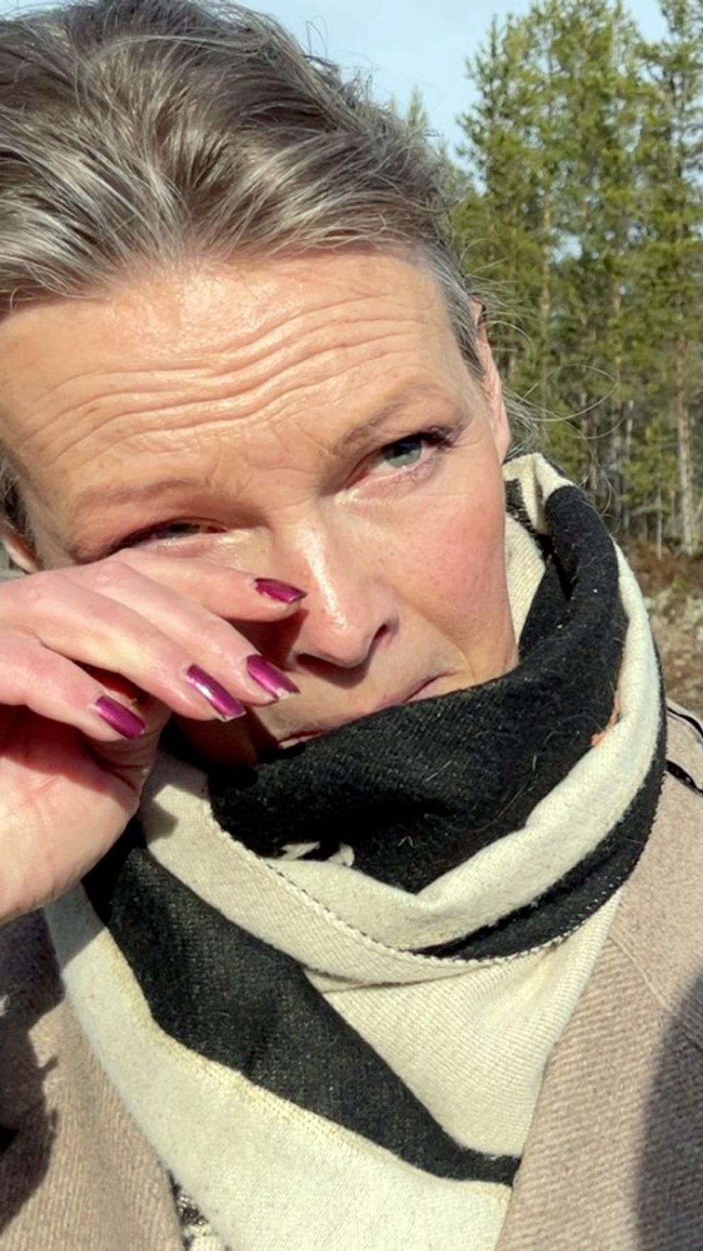 En kvinna i beige kappa torkar en tår under en intervjusituation bredvid en väg vid gränsen mot Norge.