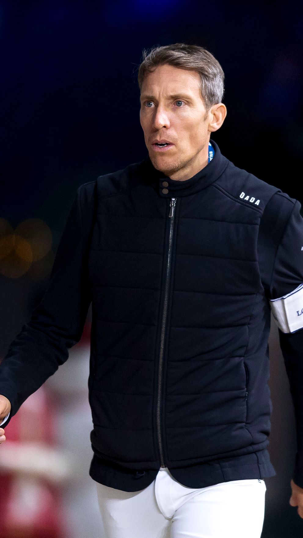 Person i svart jacka och vitt armband går på evenemang med oskarp bakgrund av ljus och publik.