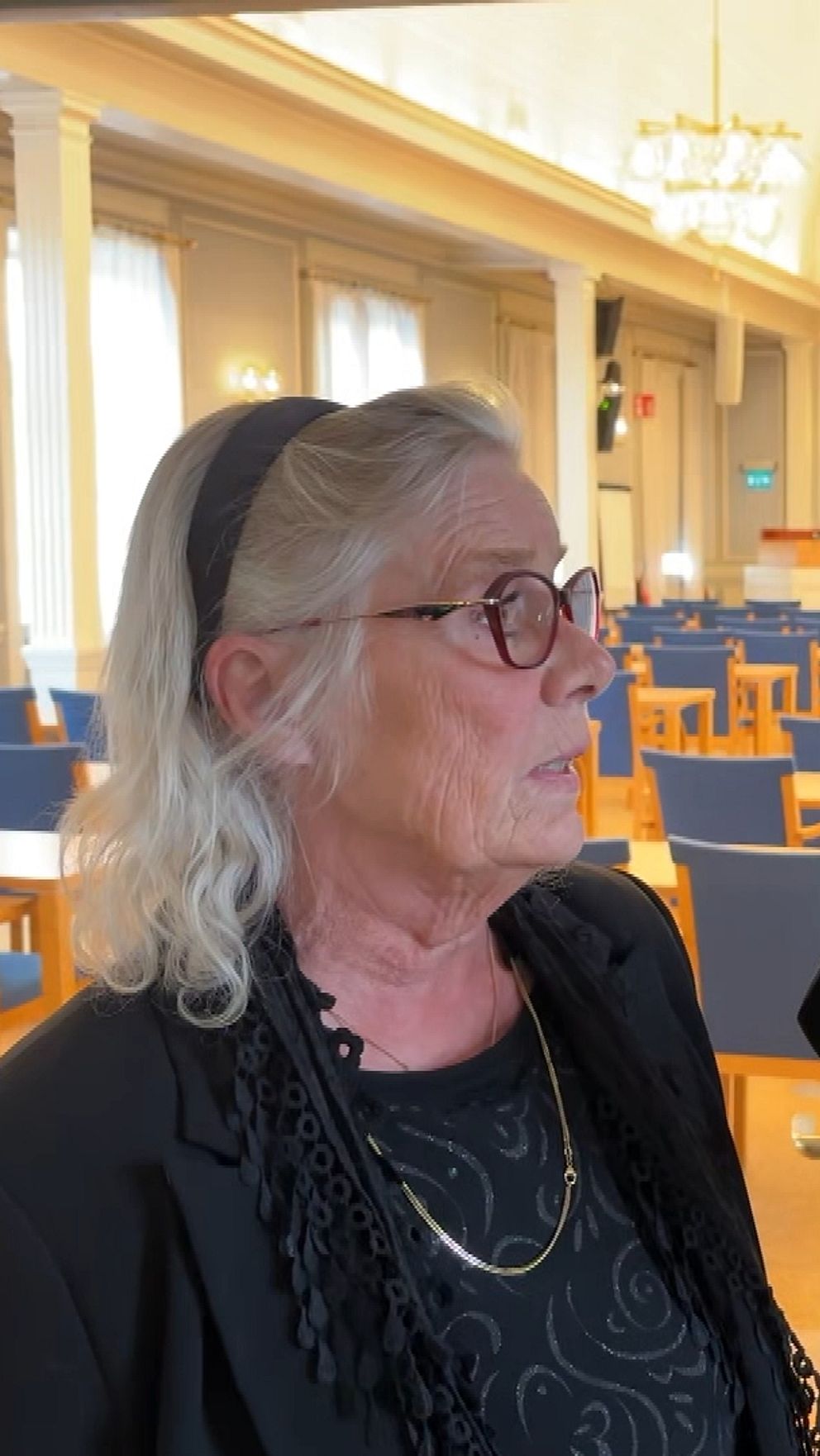 En reporter håller en mikrofon vid en intervju inne i en ljus samlingssal.