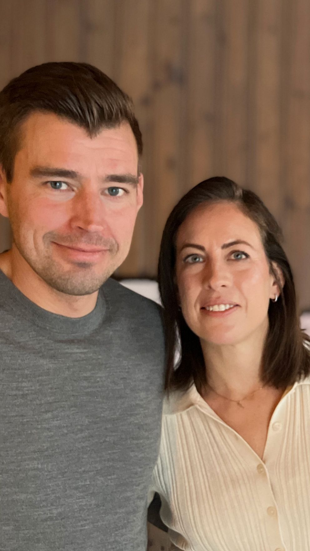 Henrik och Isabell står och håller om varandra i sitt hem och tittar in i kameran. På ena sidan syns en rund spegel i ett modernt hem.