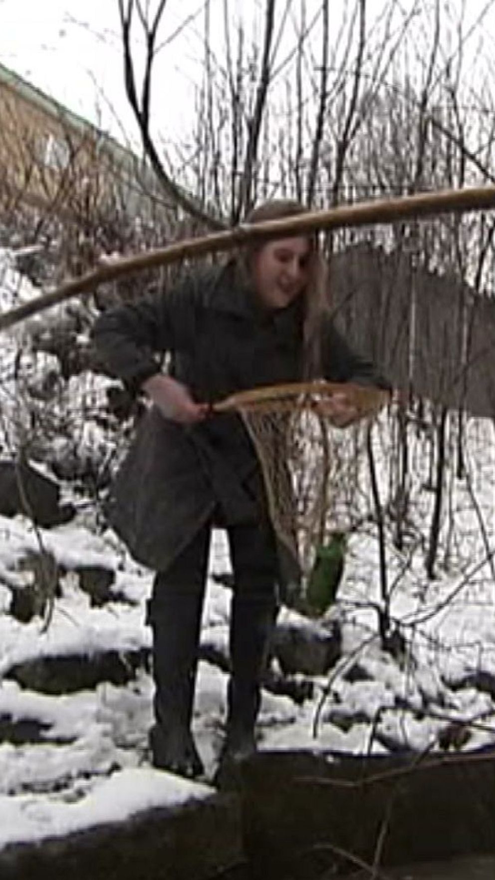 En person rensar bort sly vid ett snötäckt område med träd och en gångbro.