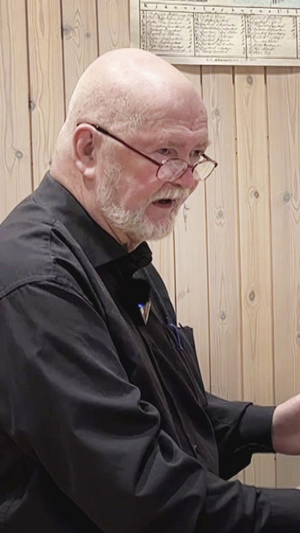 Man gestikulerar mot datorskärm i träpanelklätt rum.
