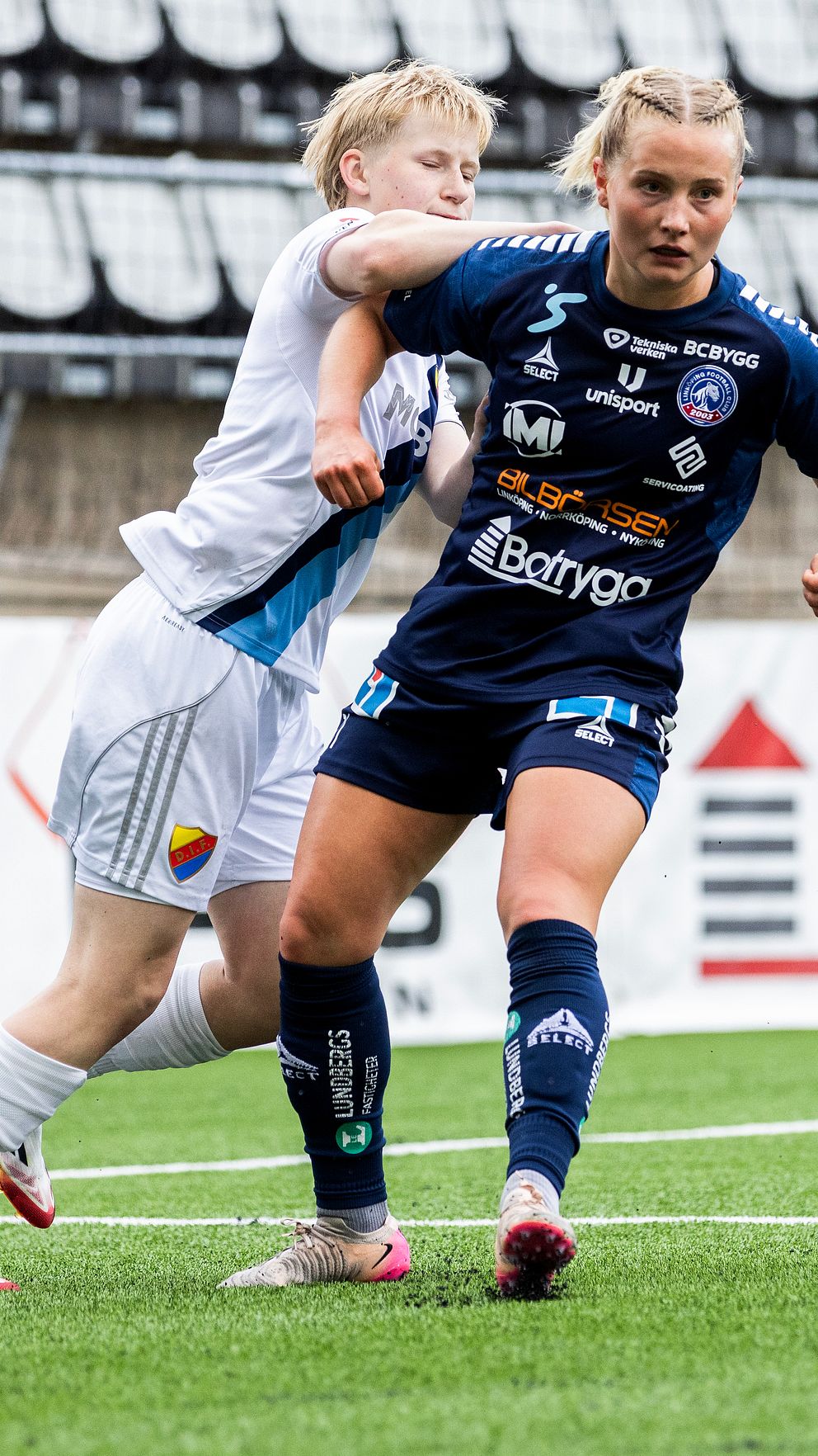 Två damfotbollsspelare kämpar om bollen på planen under en match.