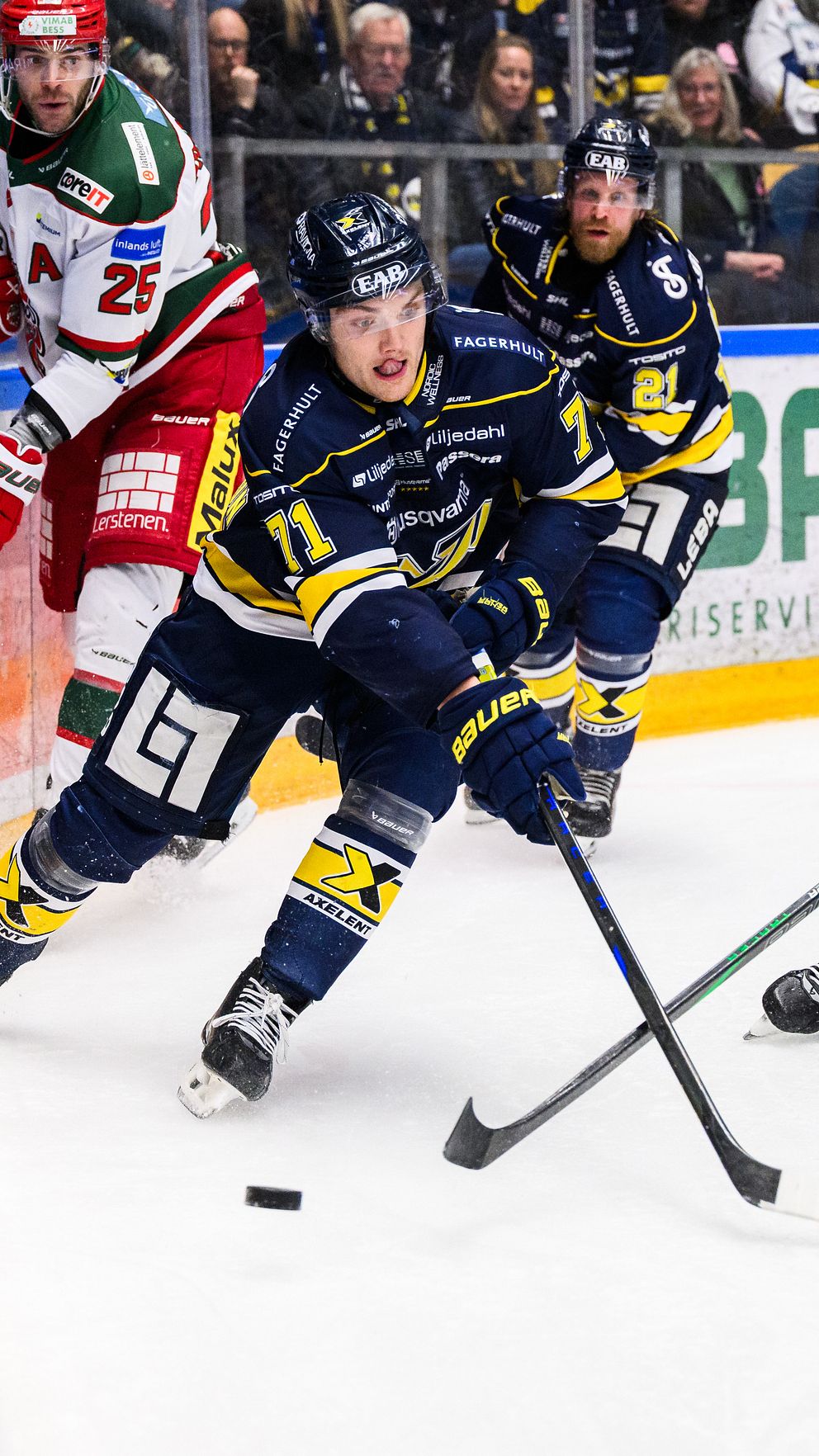 Ishockeymatch mellan spelare i blå och röda tröjor som kämpar om pucken.