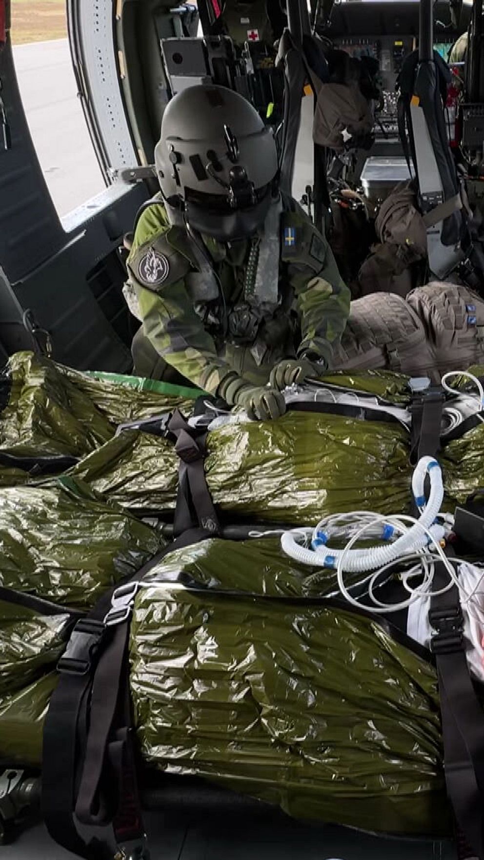 Soldater transporteras på bår inuti en militärhelikopter, vårdpersonal arbetar runt dem.