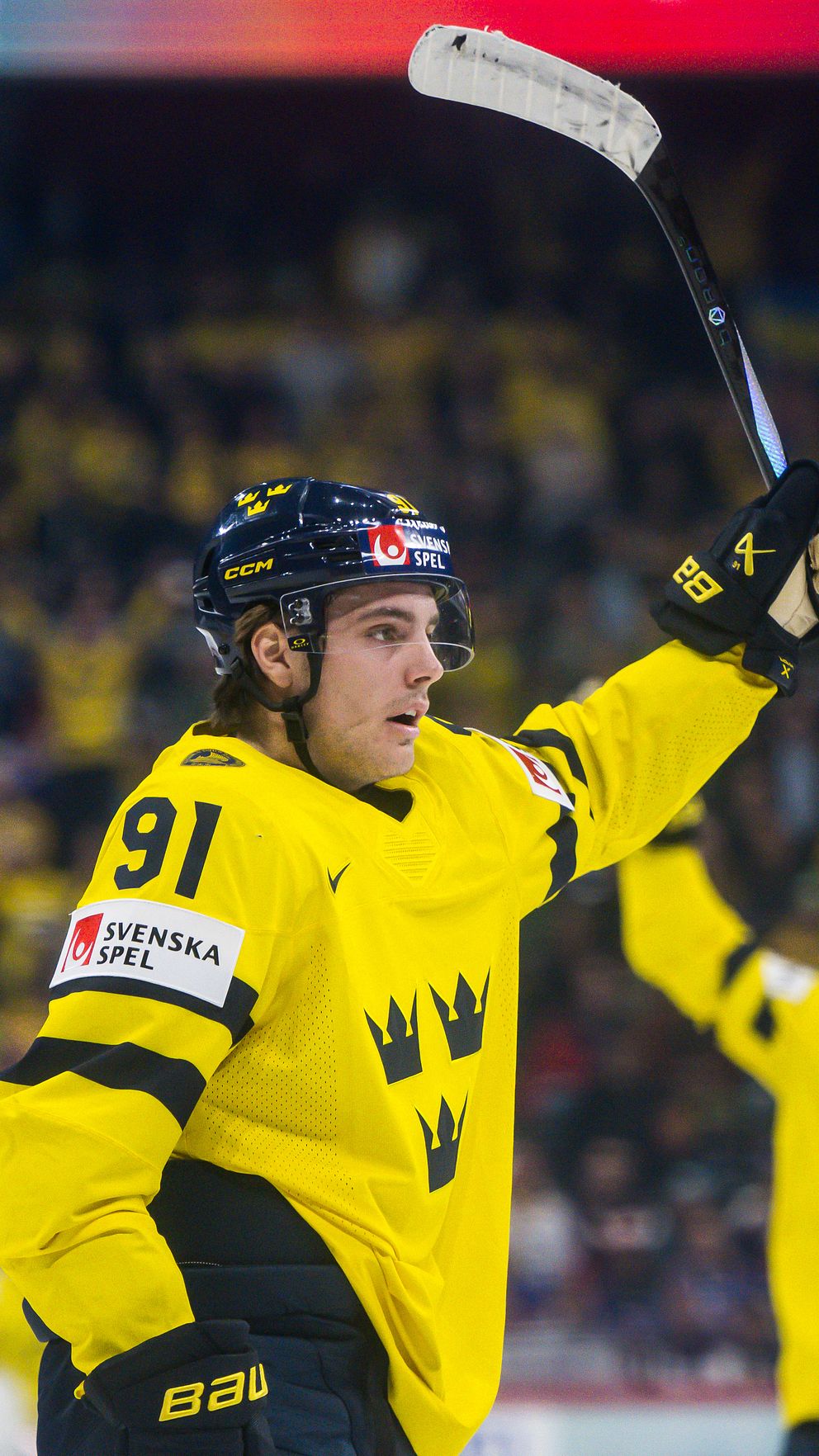 Ishockeyspelare i Tre Kronor-tröja jublar efter mål under match inför stor publik.
