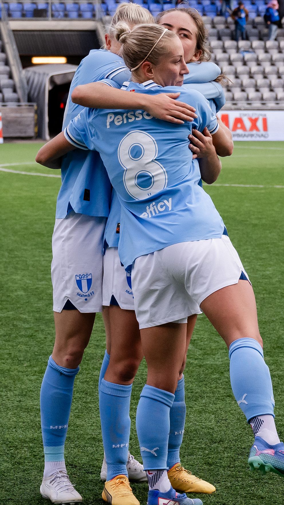 Tre spelare i MFF-tröjor kramar varandra på en fotbollsplan.