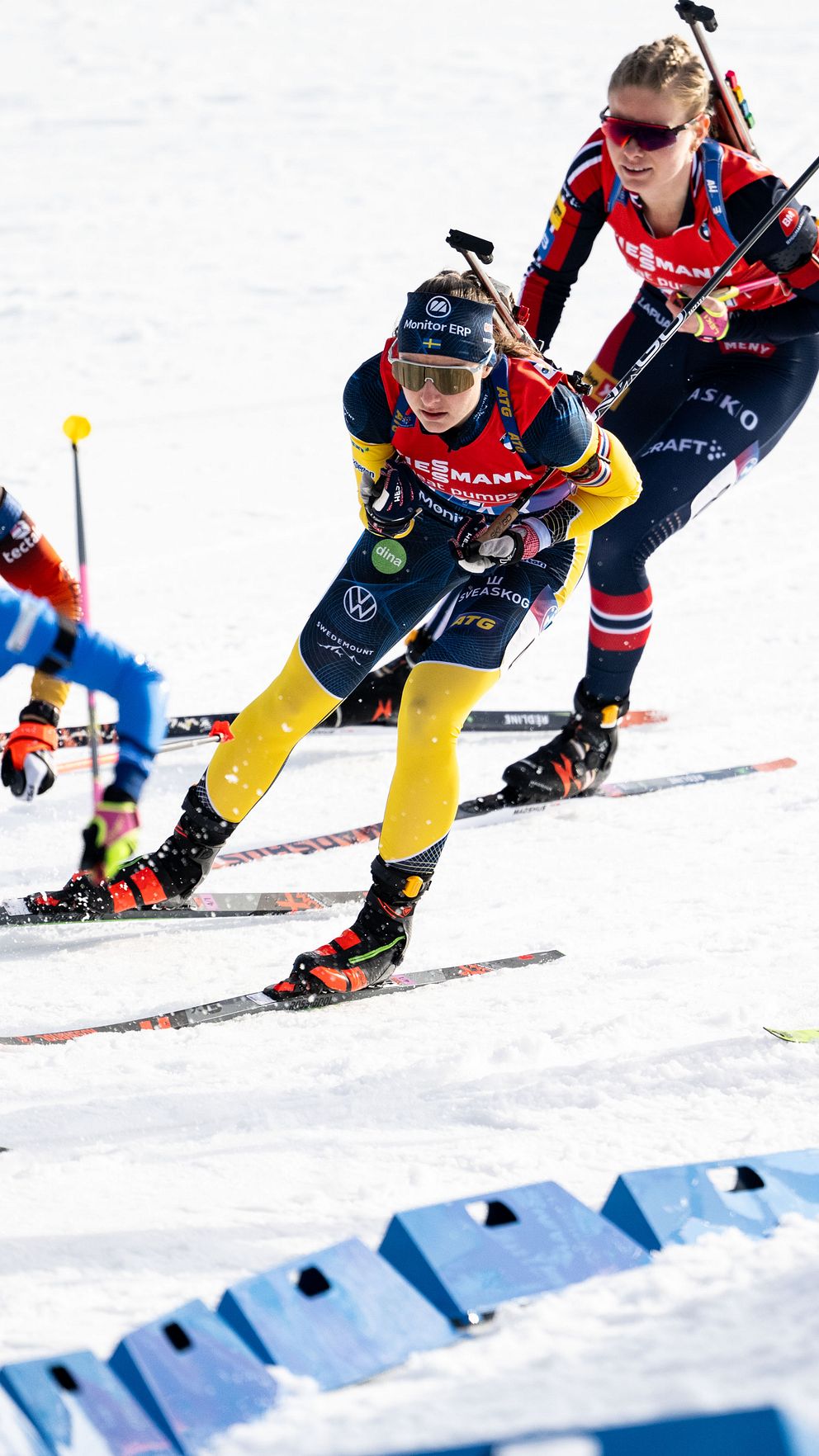 Skidskyttar i färgglada dräkter åker i grupp på snötäckt bana.
