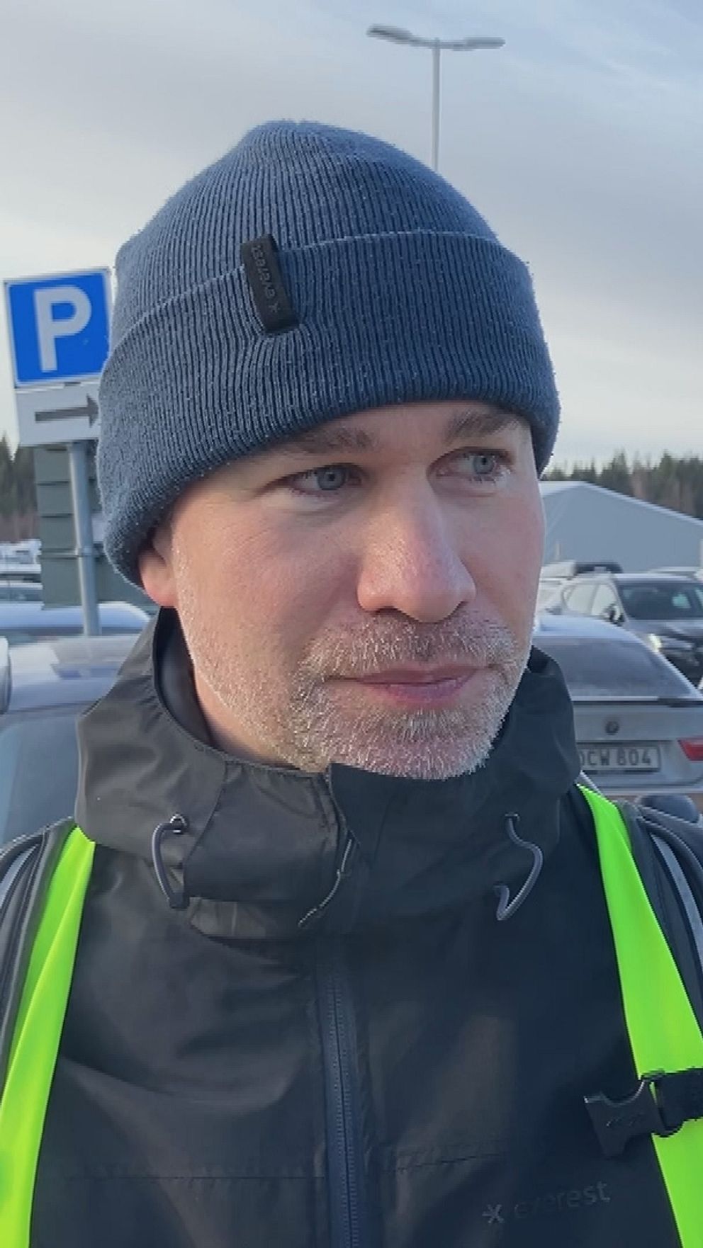 Aleksei Matrosov i reflexväst på en bilparkering utanför Northvol i Skellefteå. Flera bilar i bakgrunden.