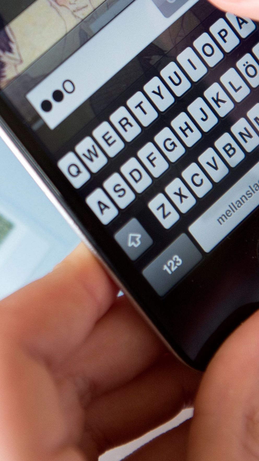 Två händer som skriver in ett lösenord på en mobiltelefon.