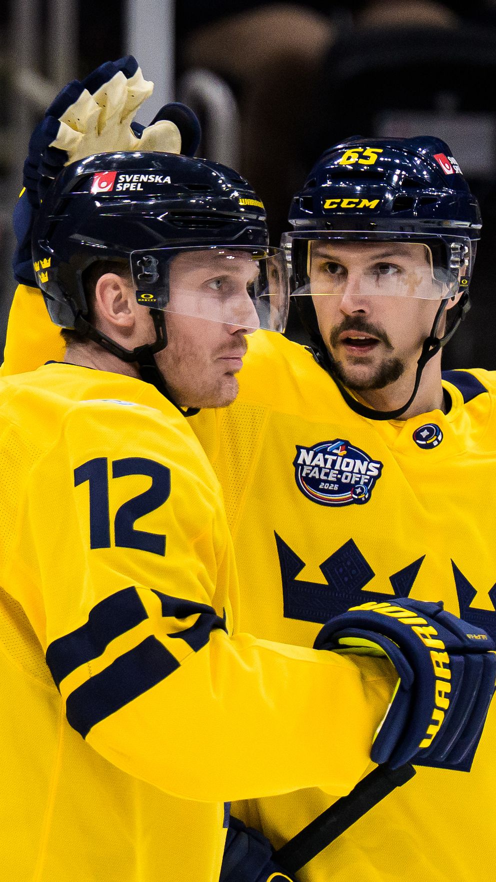 Två svenska ishockeyspelare i gula tröjor firar på isen.