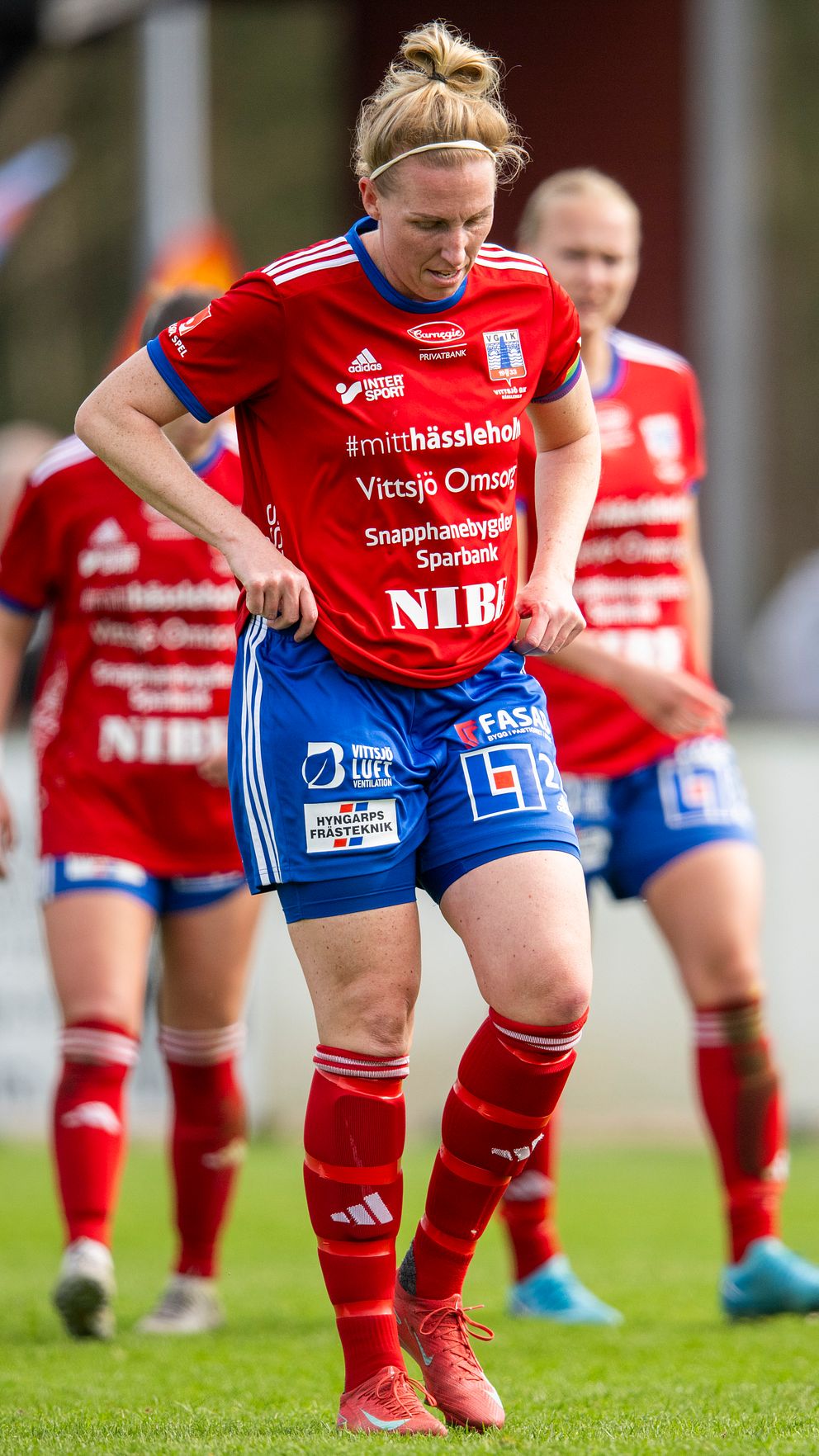 Kvinnliga fotbollsspelare i röda matchställ går samlade på fotbollsplanen.